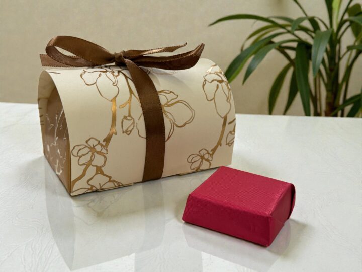 Off-white Belgian chocolate favor box with brown ribbon and wrapped chocolate piece